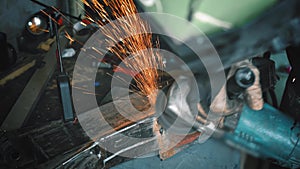 Man working with rotary angle grinder at workshop, closeup detail, orange sparks flying around