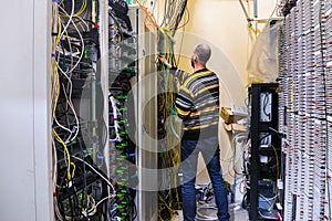 The man is working in the server room of the data center. The engineer connects the wires to provide Internet communication. The