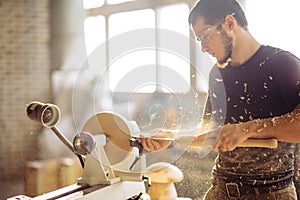 Man working at small wood lathe, an artisan carves piece of wood