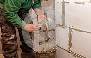 A man is working on a wall, using a trowel to apply a layer of cement