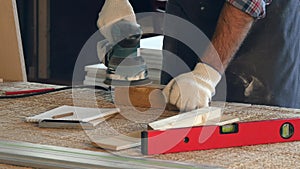 Man working with wooden planck and electric planer in workshop.