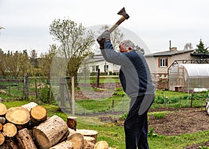 A man works with an ax in his yard, processing firewood for the winter season, burning firewood