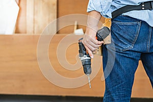 Man works in carpentry workshop. Handyman manual worker in tools belt and holding drill in his hands