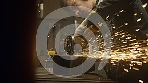 A man works with a circular saw. Worker grinder grinds metal in workshop. Sparks fly from hot metal. The man worked hard on the