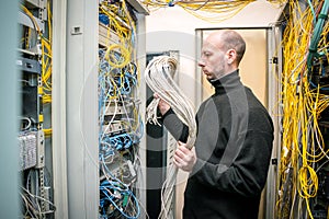 A man works with communication cables in a data center. The signalman fixes many wires to the computer racks. Information