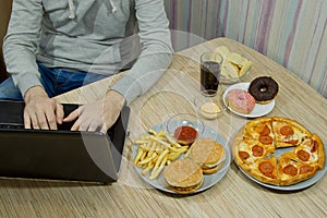 A man works at a computer and eats fast food. unhealthy food