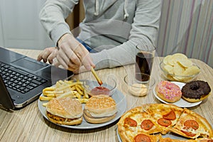 A man works at a computer and eats fast food. unhealthy food: Bu