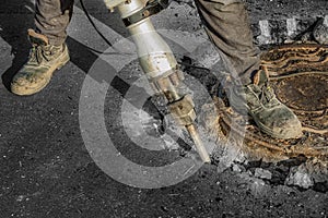 A man works with an electric jackhammer, smashes asphalt