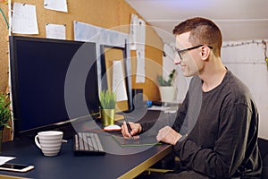 A man works at home with a tablet and pen. Griffin designer, a man looks at a green screen computer. A man works on freelance