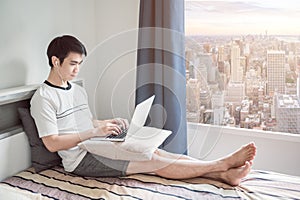 Man works from home using laptop in bedroom with aerial city view through the window