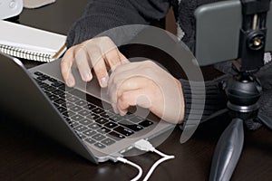 A man works at a laptop. Near the smartphone on a tripod. Hands are taken close up