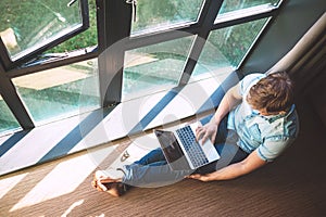 Man works with laptop sitting on the floor near the open window