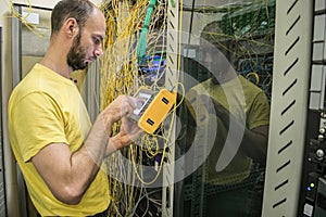 The man works in the server room of the datacenter. A technician measures the signal level in a fiber optic cable. The system