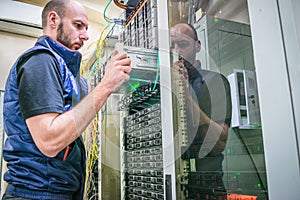 A man works in a server room. Technician repairs the central router. System administrator installs a new server in a modern data