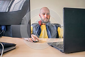 The man works at several server computers in the office. The specialist is sitting in a chair in front of two displays. An office