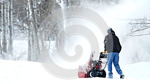 Man works with a snow blower to remove newly fallen snow from driveway