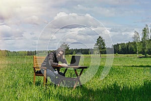 A man works at a table with a laptop in an empty field. Remote work in the field