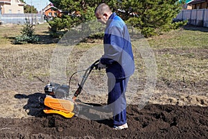 A man works in a vegetable garden in early spring. Digs the ground. Works as a cultivator, walk-behind tractor