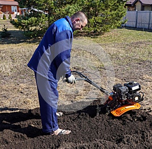 A man works in a vegetable garden in early spring. Digs the ground. Works as a cultivator, walk-behind tractor