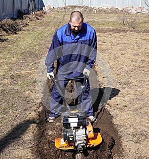 A man works in a vegetable garden in early spring. Digs the ground. Works as a cultivator, walk-behind tractor