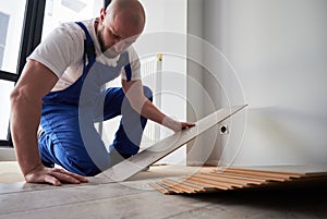 Man in workwear installing laminate flooring in apartment.