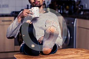 Man with worn out socks having coffee in kitchen