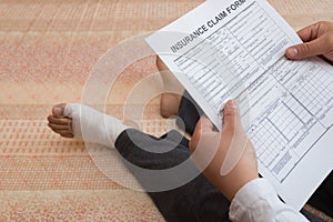 Man with a wrapped foot sitting on bed reading a work insurance claim form