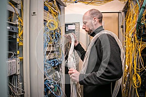 A man wrapped in many cables works in the server room. A technician is trying to understand the operation of a tangled network
