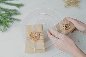 A man wraps a Christmas present in craft paper on a white wooden background