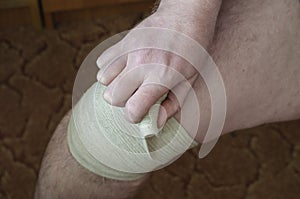 The man wraps an elastic bandage around his knee himself