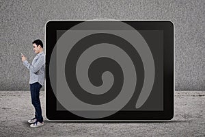 A man writes an SMS and standing by a big tablet