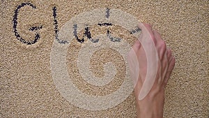 A man writes text on a black background using quinoa seeds. He writes text GLUTEN FREE