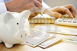 Man writing in an accounting book, piggy bank and dollar bills. Savings concept.