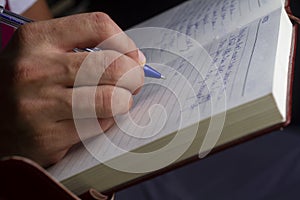 A man is writing with a blue pen on a notebook.selective focus