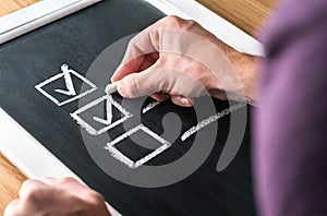 Man writing checkmark to checklist on blackboard. Document of finished work and completed tasks on chalkboard. photo