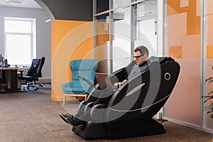 Man writing code while sitting in armchair in the office