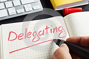 Man is writing delegating in the notepad. Delegate concept.