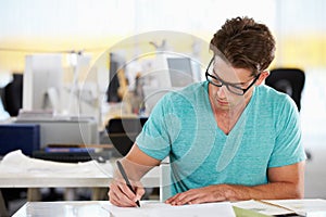 Man Writing At Desk In Busy Creative Office