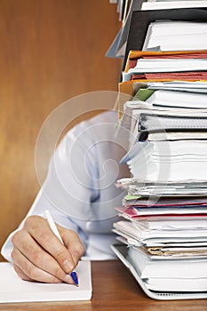 Man Writing Document Behind A Stack Of Folders