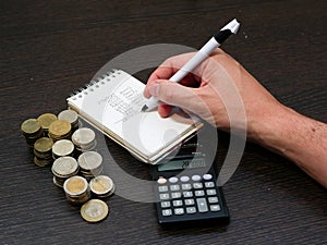 Man writing down on a notebook while counting colombian currency coins of different nominations over a table with a calculator