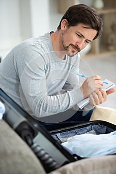 man writing list while packing suitcase photo