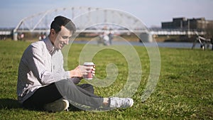 A man writing massage, outdoors and drinks coffee. Student sitting on grass chating. Handsome businessman writing massages with pa