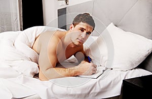 Man writing a note in his bed.