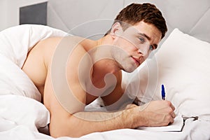 Man writing a note in his bed.