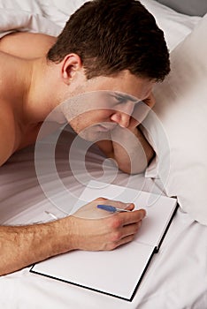 Man writing a note in his bed.