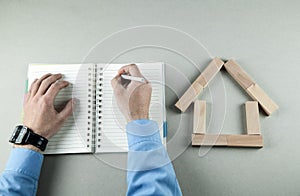 Man writing on notepad. House model made of wooden blocks