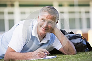 A man writing notes while lying on a campus lawn