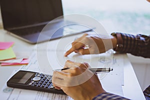 Man Writing paper and using calculator Calculating bonusOr other compensation to employees to increase productivity. on desk.