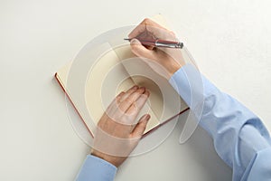 Man writing with pen in notebook at white table, top view