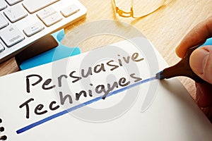 Man writing Persuasive Techniques in a note. photo